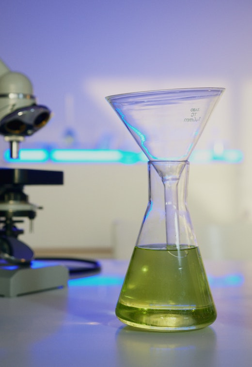 Blue light being beamed into a glass funnel inserted into an Erlenmeyer flask of clear green solution.