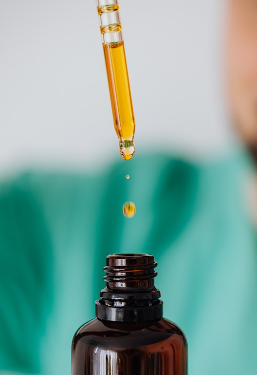 A pipette dispensing orange solution into a brown bottle.