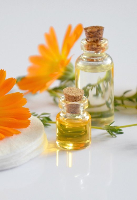 Two corked glass bottles of essential oil in front of orange flowers.