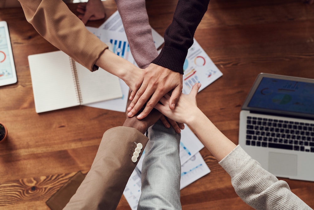 Six hands stacked on top of one another in a gesture of teamwork.