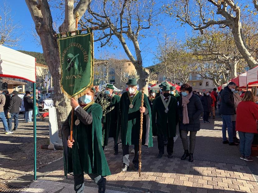 A parade of people wearing green and holding a green pendant with olives on it.