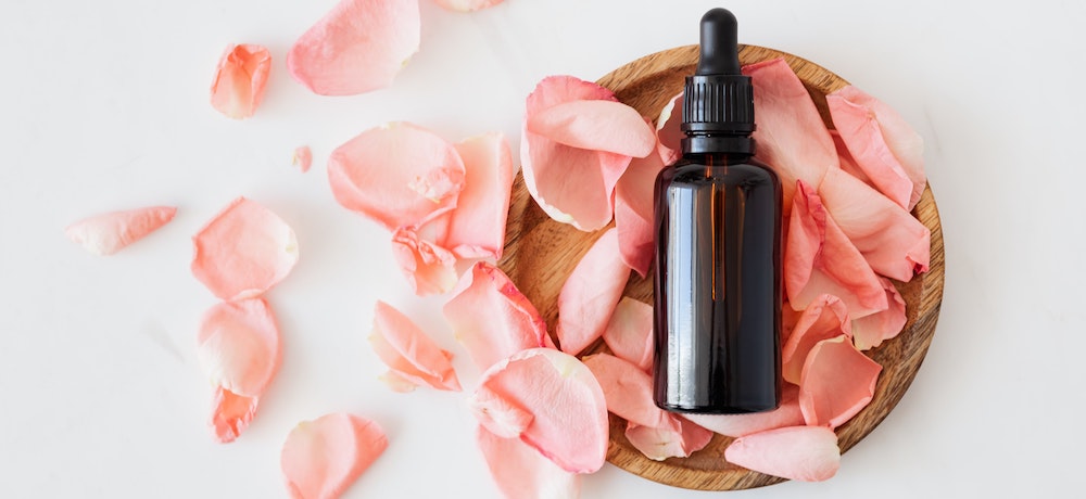 A bottle of essential oil lying in a bowl of pink flower petals.