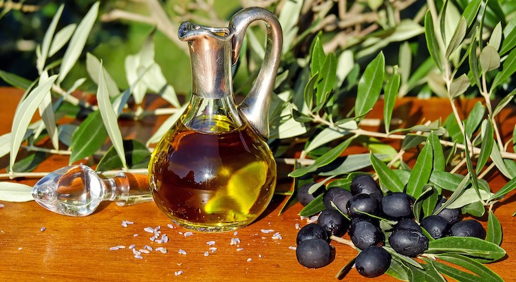 Black olives next to a glass pitcher of olive oil.